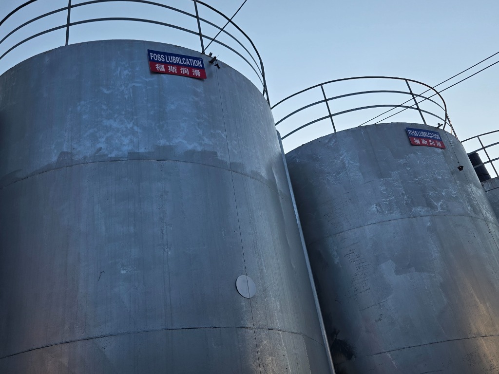 Giant outdoor bulk base oil storage silos against blue sky with FOSS LUBRICATION registered brand plates