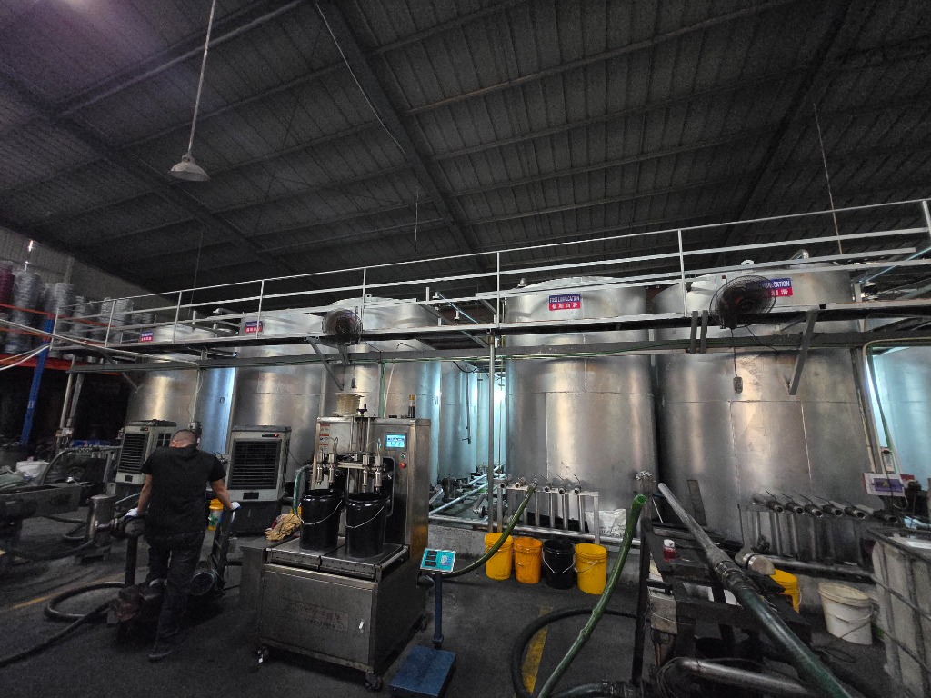Operator managing semi-automated digital load-cell weighing and dual-nozzle filling machine in front of blending kettles