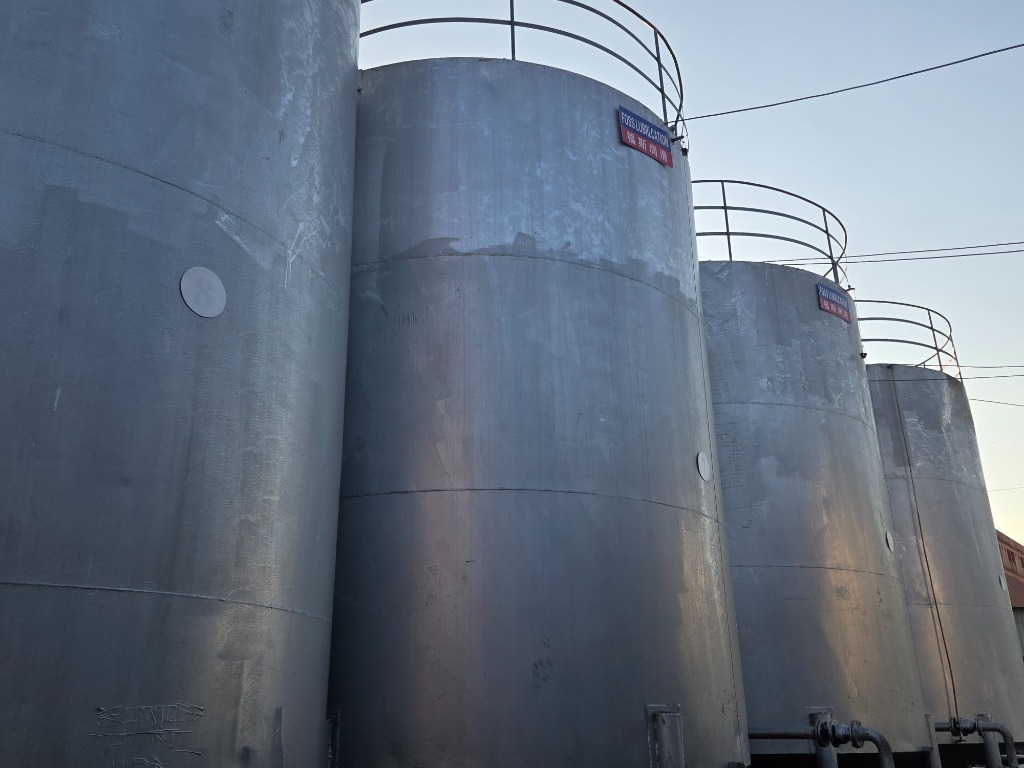 Battery of outdoor vertical bulk storage tanks numbered 5 to 8 with bottom discharge pipe manifolds